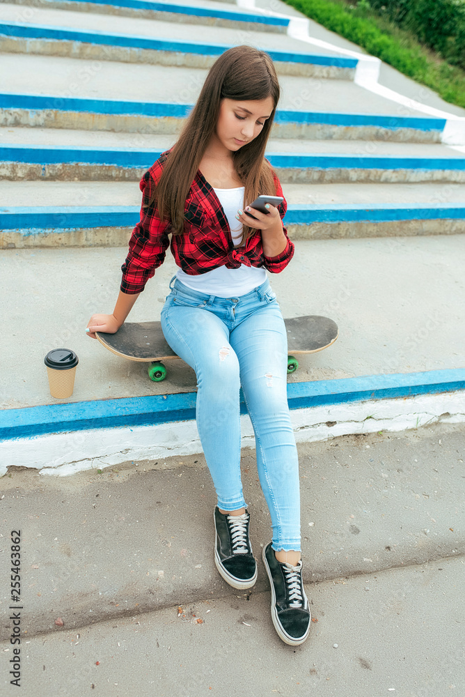 Girl schoolgirl 13-16 years old sits on a skateboard stairs in her hand  phone, a