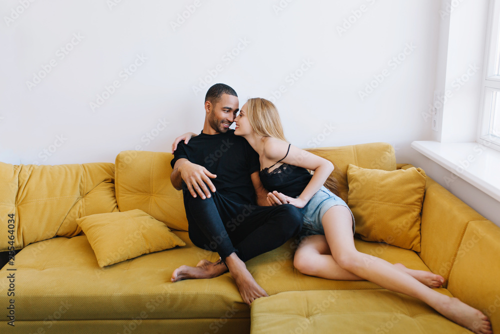 Couple flirting, holding hands, showing love, touching noses, look in the eyes. Loving pair sitting together on the couch. Romance, love relationships, happy faces. Couple flirting, holding hands, showing love, touching noses, look in the eyes. Loving pair sitting together on the couch. Romance, love relationships, happy faces.