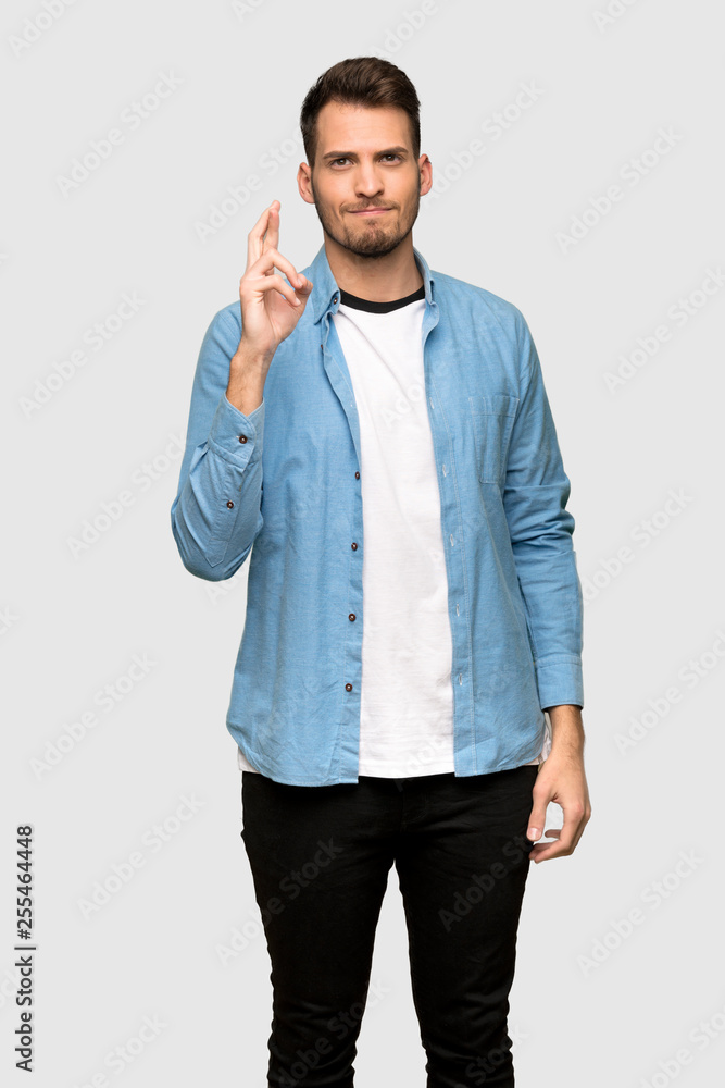 Handsome man with fingers crossing and wishing the best over grey background Handsome man with fingers crossing and wishing the best over grey background