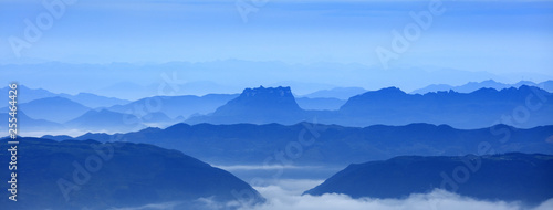 Abstract Image, Mountain Silhouettes at dawn - rolling jagged mountain peaks, cold blue color hues. Panoramic Abstract Background Image, overcast skies, layers of rolling mountains in the distance. © Cedar
