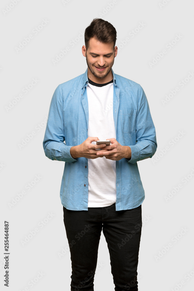 Handsome man sending a message with the mobile over grey background Handsome man sending a message with the mobile over grey background
