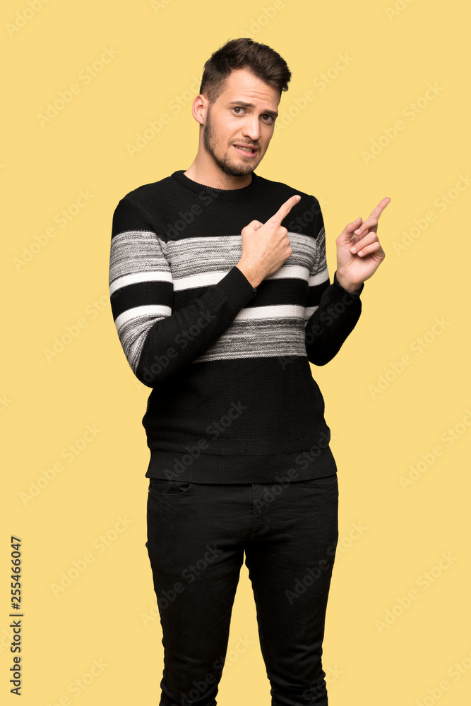 Handsome man frightened and pointing to the side over yellow background Handsome man frightened and pointing to the side over yellow background