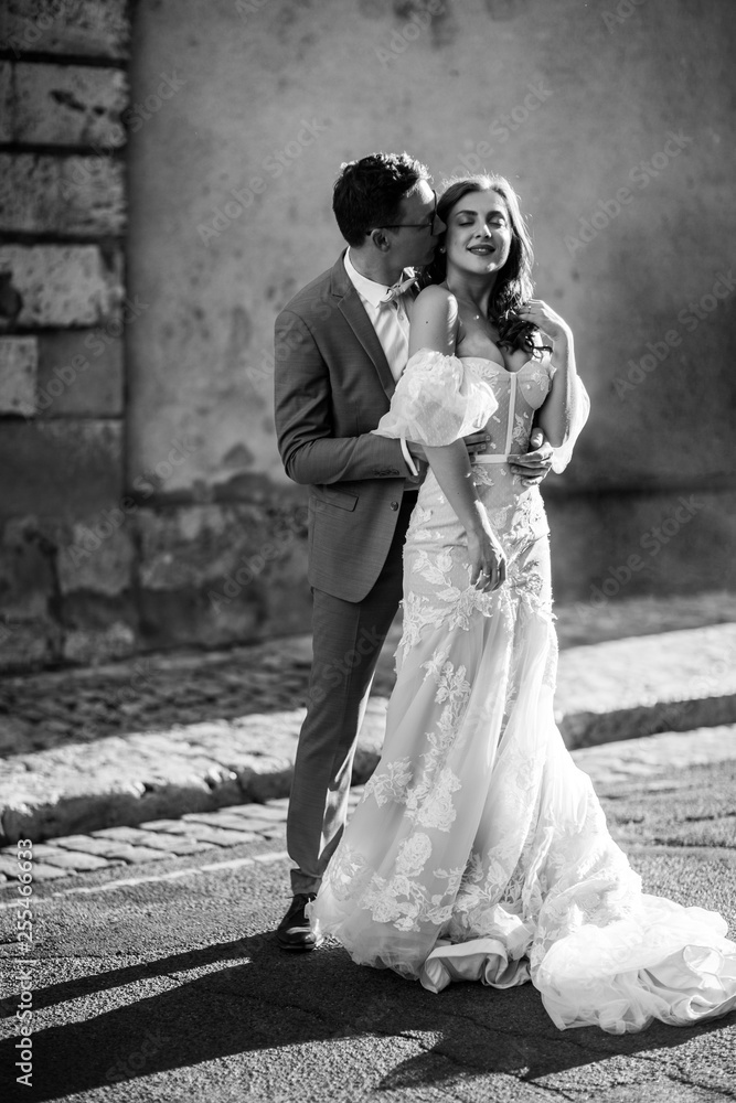 Happy newlyweds. The groom hugs and kisses his beloved beautiful bride, outdoors. Black and white photo
