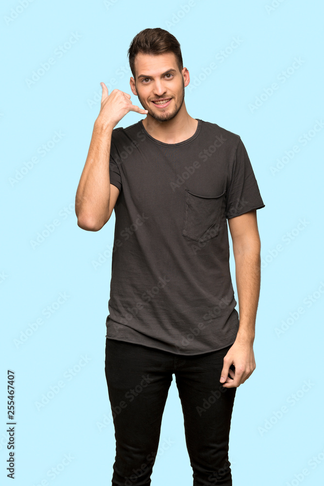 Man with black shirt making phone gesture. Call me back sign over blue background Man with black shirt making phone gesture. Call me back sign over blue background