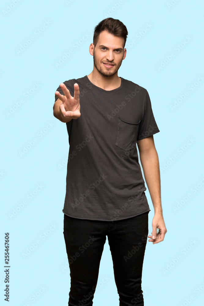 Man with black shirt happy and counting three with fingers over blue background Man with black shirt happy and counting three with fingers over blue background