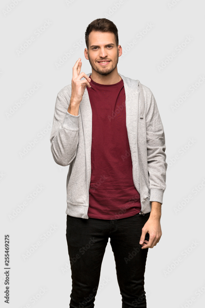 Man with sweatshirt with fingers crossing and wishing the best over grey background Man with sweatshirt with fingers crossing and wishing the best over grey background