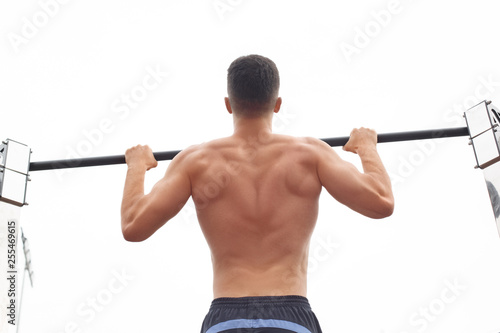 Healthy Lifestyle. Young man shirtless exercising outdoors pull-up on bar back view