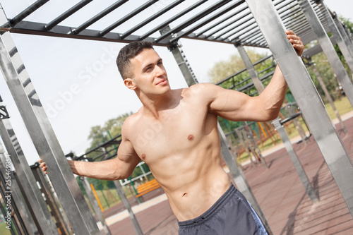Healthy Lifestyle. Young man shirtless standing outdoors leaning on bars looking aside happy