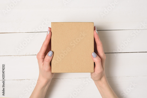 Small cardboard box in female hands. Top view. White table on the background © somemeans