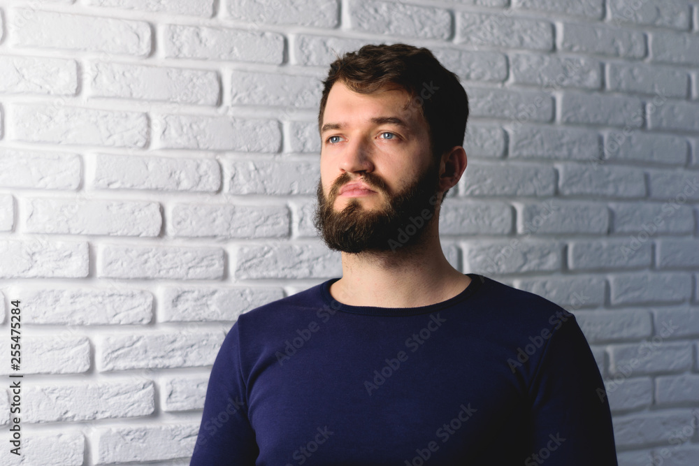 Fototapeta premium portrait of a handsome bearded man on brick wall background. Pensive hipster isolated