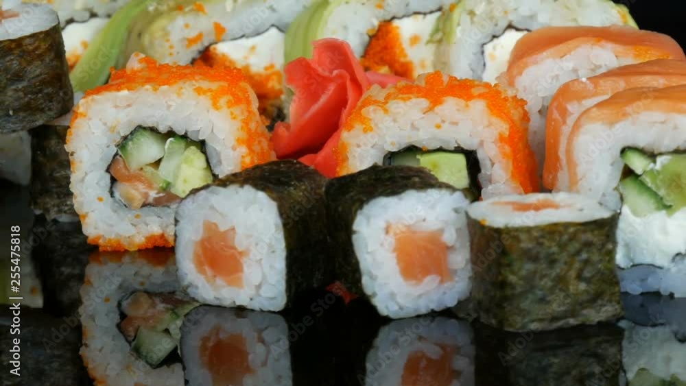 A variety of colored sushi rolls sets and ginger rotate on the mirror surface on a black background. Japanese cuisine in the studio A variety of colored sushi rolls sets and ginger rotate on the mirror surface on a black background. Japanese cuisine in the studio
