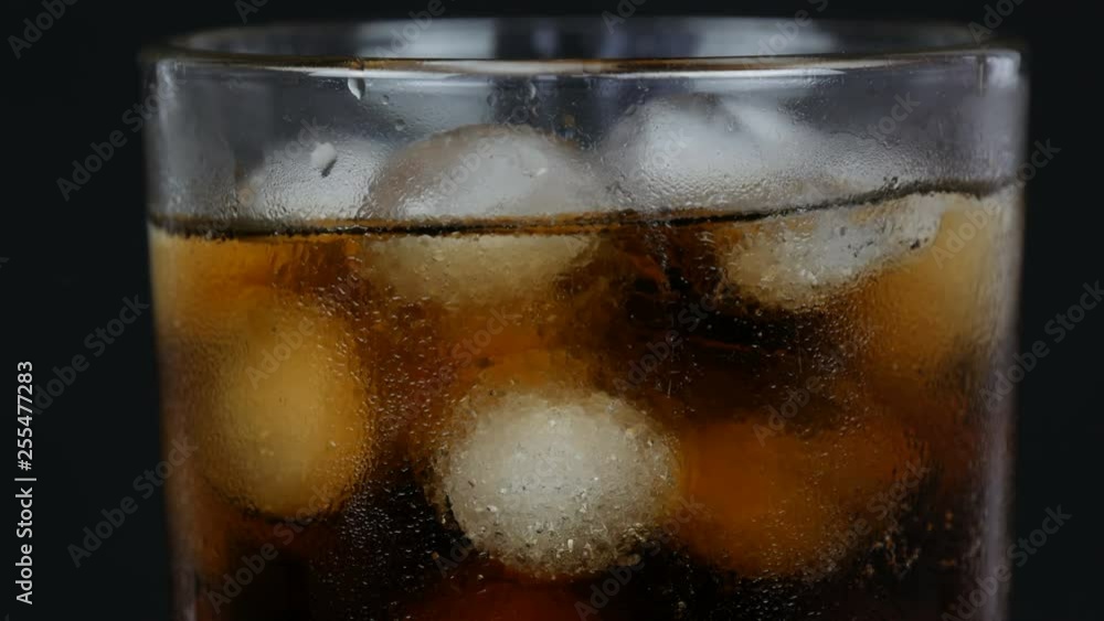 Bubbles of cold cola in a transparent long glass with ice on a black background close up view Bubbles of cold cola in a transparent long glass with ice on a black background close up view