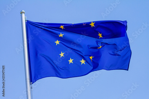 Flag of the European Union waving in the wind on flagpole against the sky with clouds on sunny day, close-up