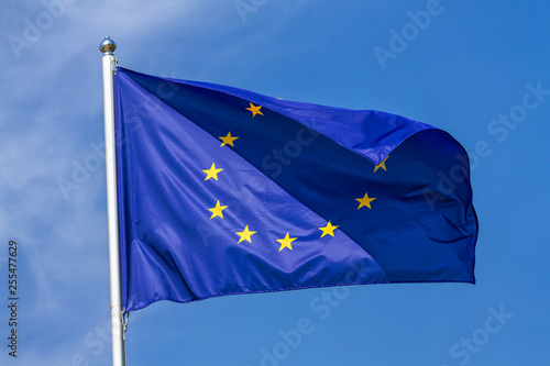 Flag of the European Union waving in the wind on flagpole against the sky with clouds on sunny day, close-up