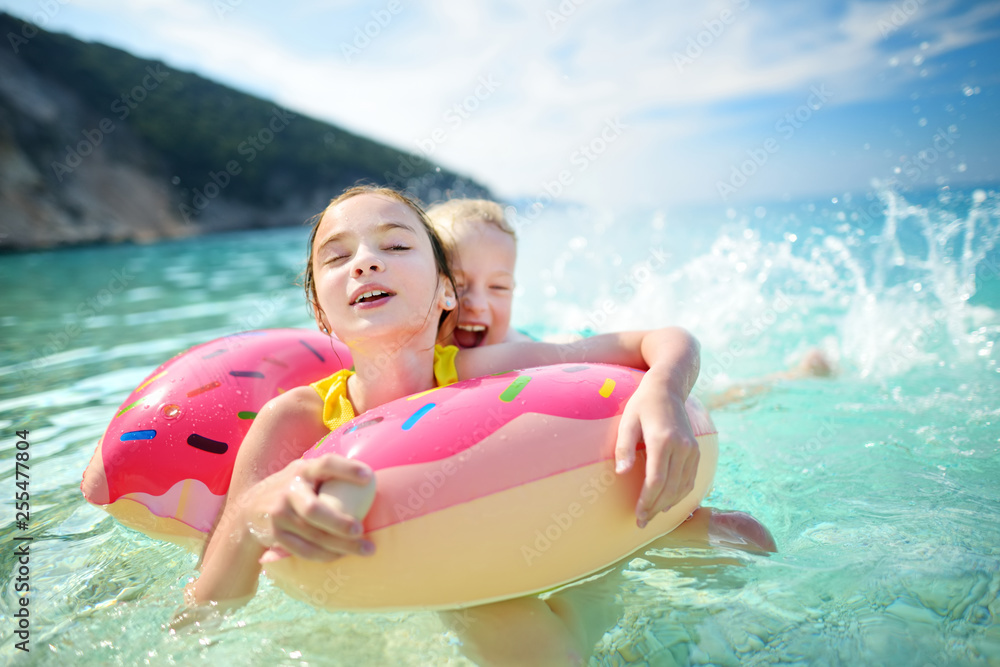 © MNStudio - Cute young sisters floating on toy ring at Myrtos beach, the most famous and beautiful beach of Kefalonia, a large coast with turqoise water and white coarse sand.