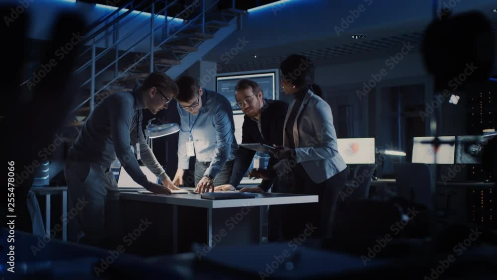 Diverse Team of Electronics Development Engineers Standing at the Desk Working with Documents, Solving Project Problems Late at Night. Specialists Working on Modern Industrial Design. Slow Motion Diverse Team of Electronics Development Engineers Standing at the Desk Working with Documents, Solving Project Problems Late at Night. Specialists Working on Modern Industrial Design. Slow Motion