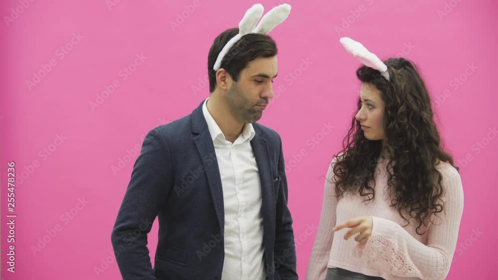 Young lovers couple on the pink background. With hackneyed ears on the head. During this, the photos of Sephi on the phone are very sincere smiles. Funny people. Young lovers couple on the pink background. With hackneyed ears on the head. During this, the photos of Sephi on the phone are very sincere smiles. Funny people.