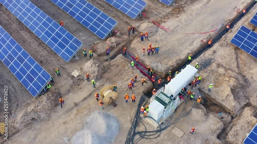 Aerial top view of a large group of workers installing a power cable in a transformer box at a giant industrial solar power station (solar electricity plant)