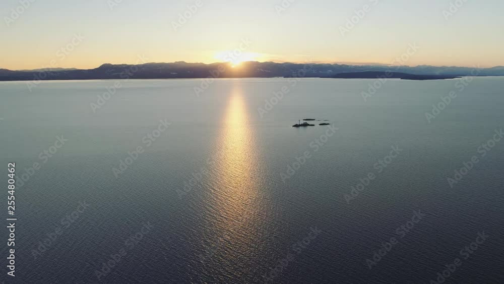 Aerial flying over ocean with island and lighthouse below. Coastal Canada at sunset. Warm golden hour. Aerial flying over ocean with island and lighthouse below. Coastal Canada at sunset. Warm golden hour.