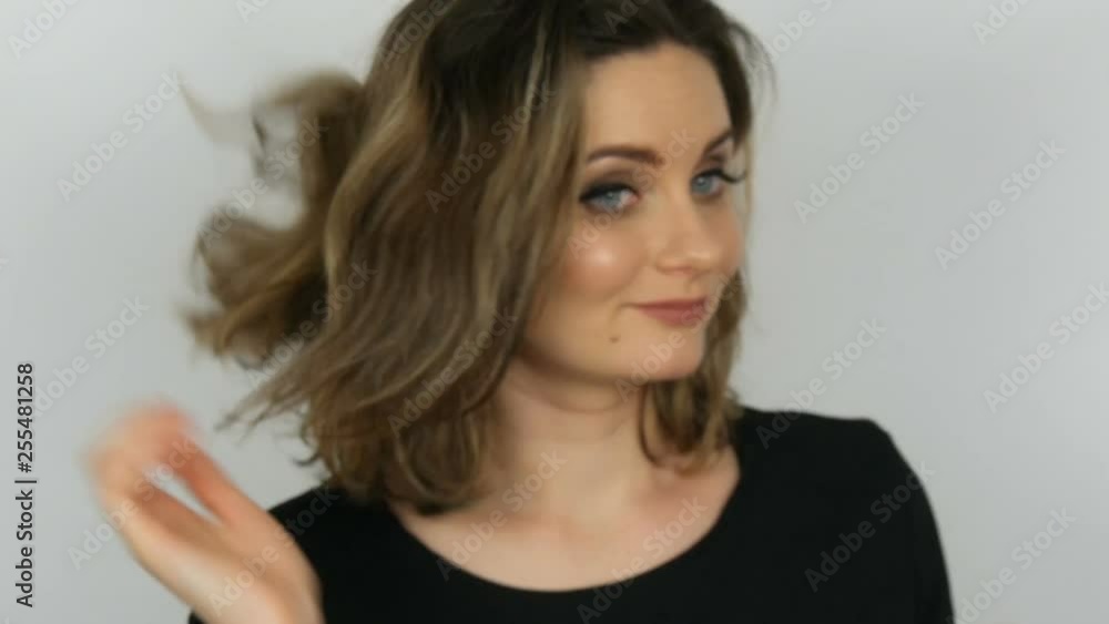 Portrait of a beautiful young sexy elegant woman in a black dress who touches her hair, straightens her hair and looks into the camera while smiling on a white background Portrait of a beautiful young sexy elegant woman in a black dress who touches her hair, straightens her hair and looks into the camera while smiling on a white background