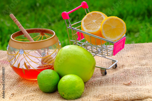 Sweet honey in the jar, shopping cart, lime  and green apple with blurred background. Conceptual image of buying vegetables and healthy eating. photo