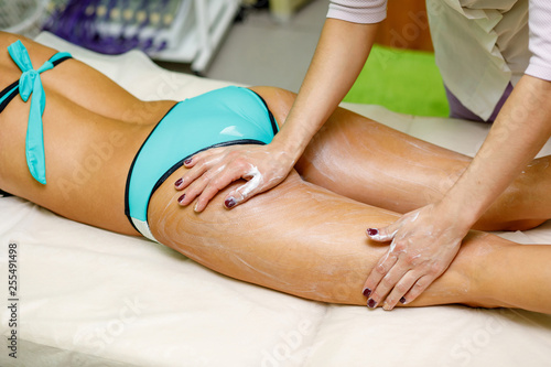Masseur applying cream to woman s thigh. Massage in spa salon