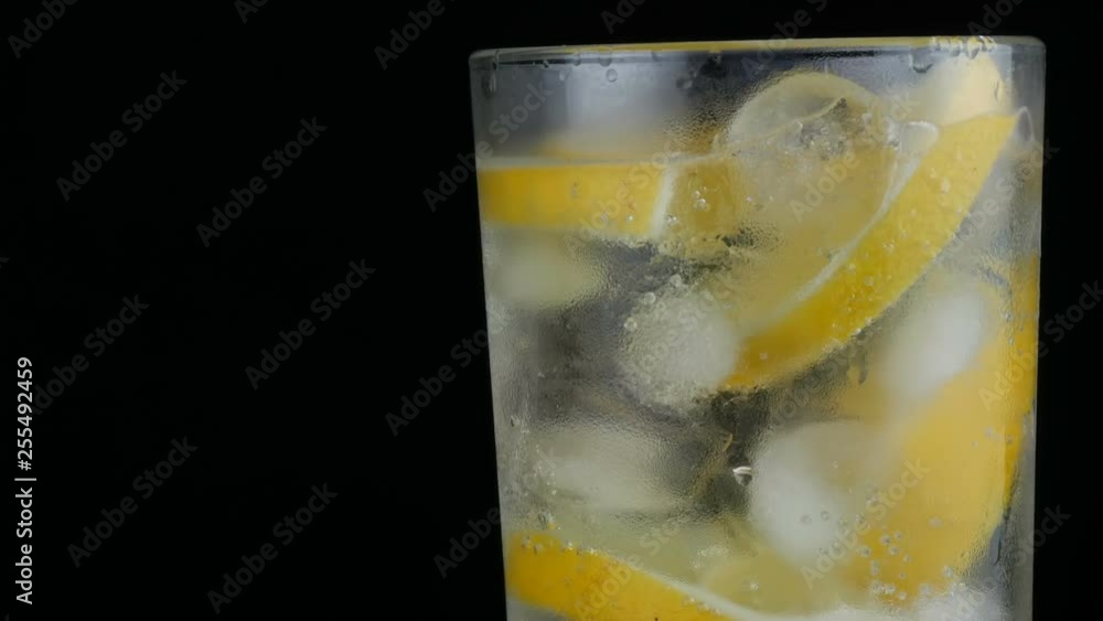 Sliced lemon in a long glass with ice cubes and cold soda on a black background close up view. Refreshing Lemonade Bubbles Sliced lemon in a long glass with ice cubes and cold soda on a black background close up view. Refreshing Lemonade Bubbles