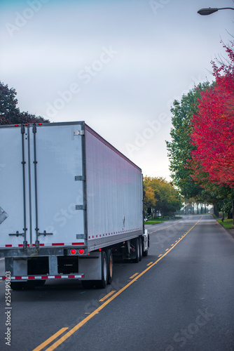 Big rig bonnet semi truck with dry van semi trailer running on autumn colorful road