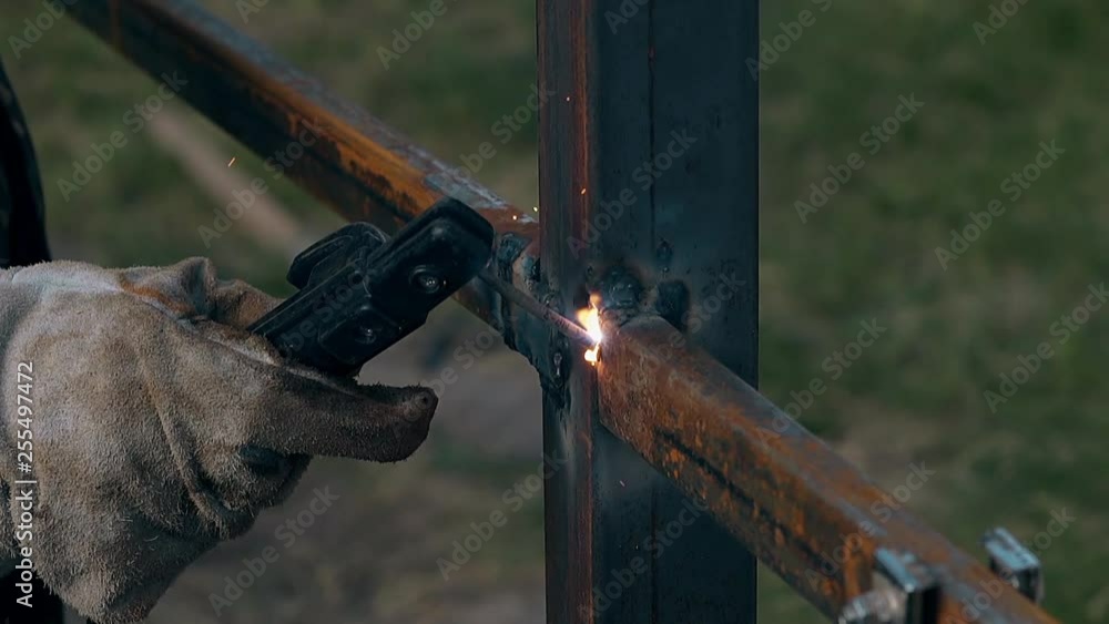 close view skilled welder builds fence with metal planks using modern tool in green yard at house close view skilled welder builds fence with metal planks using modern tool in green yard at house
