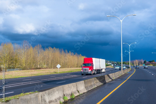 Red big rig semi truck with two semitrailers driving on divided multiline highway