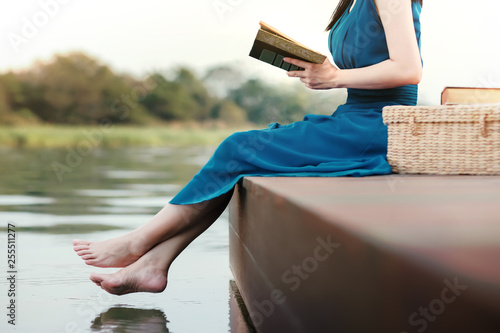 Young Woman Relaxing by Riverside. Sitting on Deck and Reading Book. Unplugged Life Concept