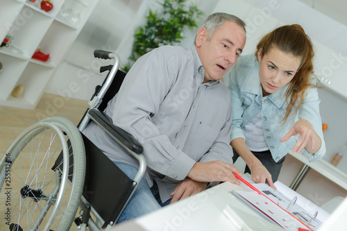 senior man in wheelchair working from home with young lady