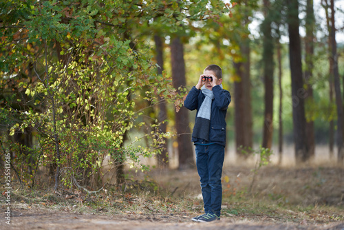 A boy with blue jacket looking through binoculars in the forest 