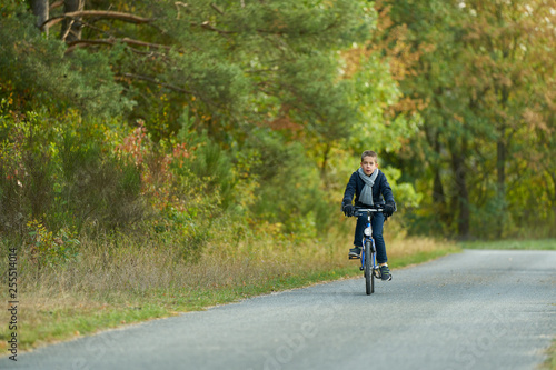 Boy with blue jacket rides a bicycle on an autumn day in the forest