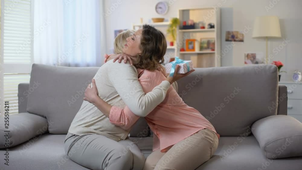 Young woman presenting gift box to mother and hugging, family care, birthday Young woman presenting gift box to mother and hugging, family care, birthday
