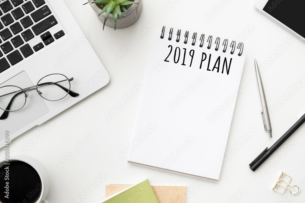 Notebook page with 2019 plan text on white office desk table. Top view, flatl lay. Notebook page with 2019 plan text on white office desk table. Top view, flatl lay.
