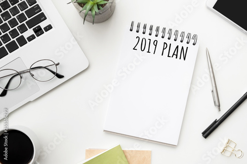Notebook page with 2019 plan text on white office desk table. Top view  flatl lay.