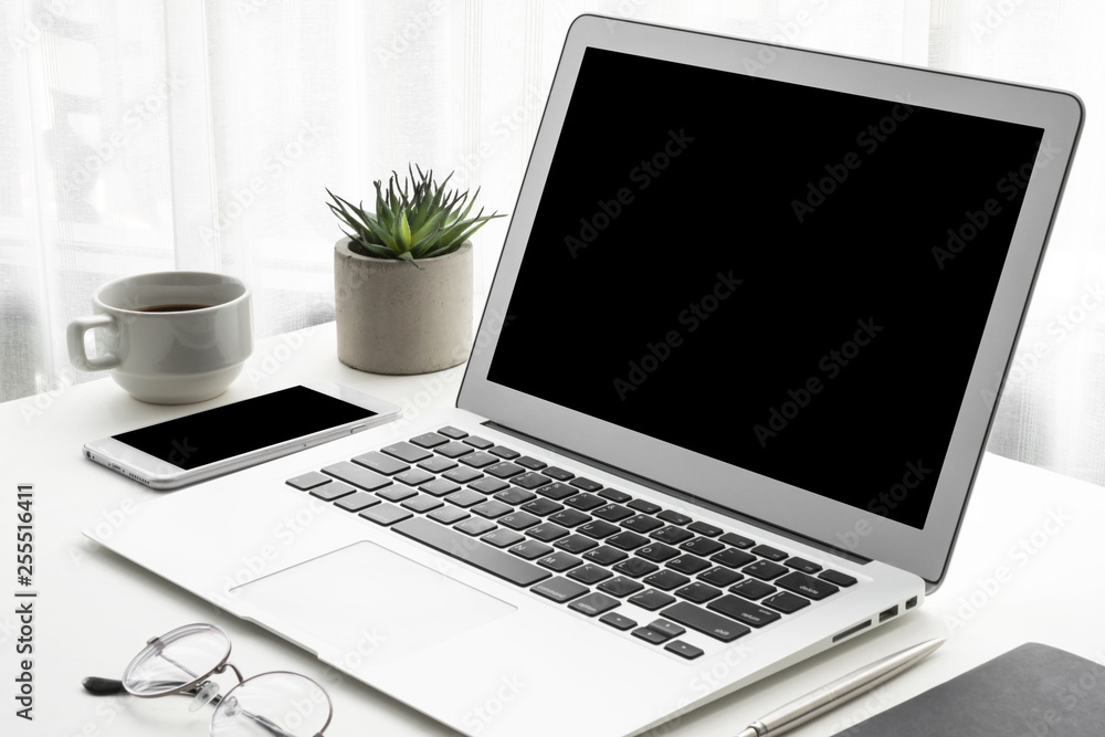 Fototapeta premium Laptop computer and smartphone with blank mock up screens are on top of white office desk table.