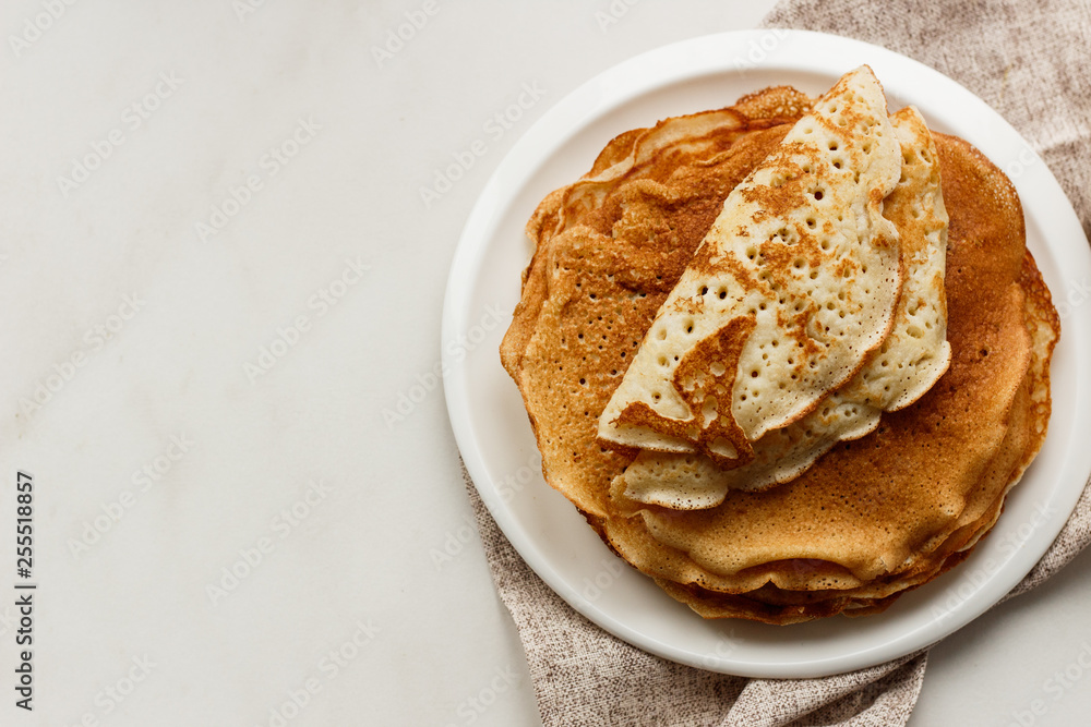 Staple of wheat golden yeast pancakes or crepes in a white plate closeup Staple of wheat golden yeast pancakes or crepes in a white plate closeup