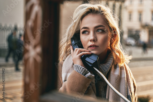 Obraz na płótnie Young beautiful blond woman making an important call in a vintage public phone booth on a sunny evening w salonie