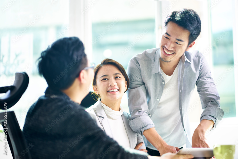 three happy asian teammates discussing business in office three happy asian teammates discussing business in office