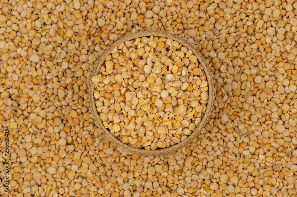 Raw yellow split peas in a wooden plate on a background of pea texture Raw yellow split peas in a wooden plate on a background of pea texture