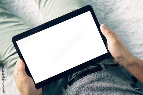 A close up of a man in a domestic surroundings holding a tablet and looking to the white blank screen. A young man looks at the screen of a digital tablet lying on the couch. Fingers off the screen photo