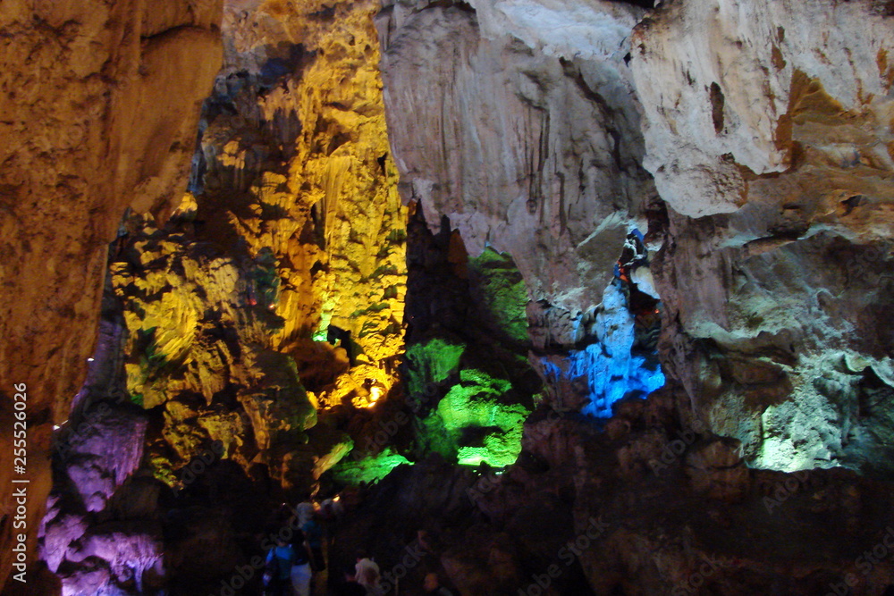 The unique landscape of stalactites and stalagmites of various shapes and sizes in the rocky caves of small islands under the rays of colorful illumination.
