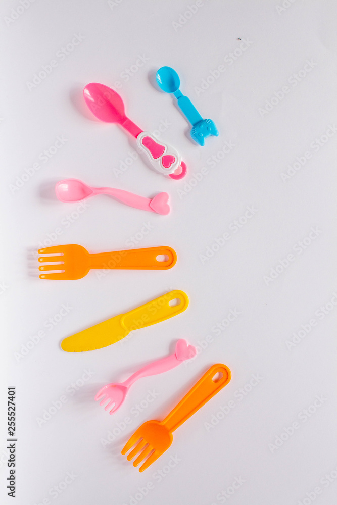 Children plastic dishes on a white background, forks, spoons, plate with space for text. Flat lay, top view minimal concept. Children plastic dishes on a white background, forks, spoons, plate with space for text. Flat lay, top view minimal concept.