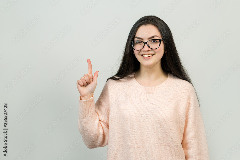 Happy young caucasian female in glasses in a pink jumper pointing fingers away, showing copy space for your text. Happy young caucasian female in glasses in a pink jumper pointing fingers away, showing copy space for your text.
