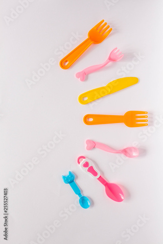 Children plastic dishes on a white background  forks  spoons  plate with space for text. Flat lay  top view minimal concept.