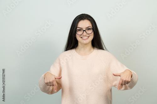 Happy young caucasian female in glasses in a pink jumper pointing fingers away, showing copy space for your text.