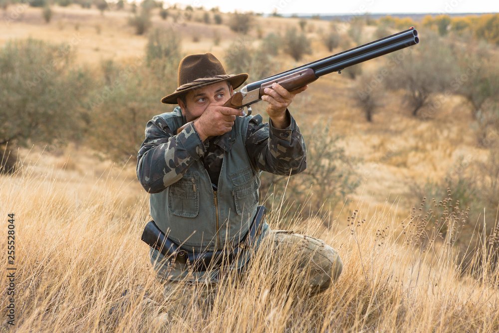 Fototapeta premium Hunter with a hat and a gun in search of prey in the steppe 