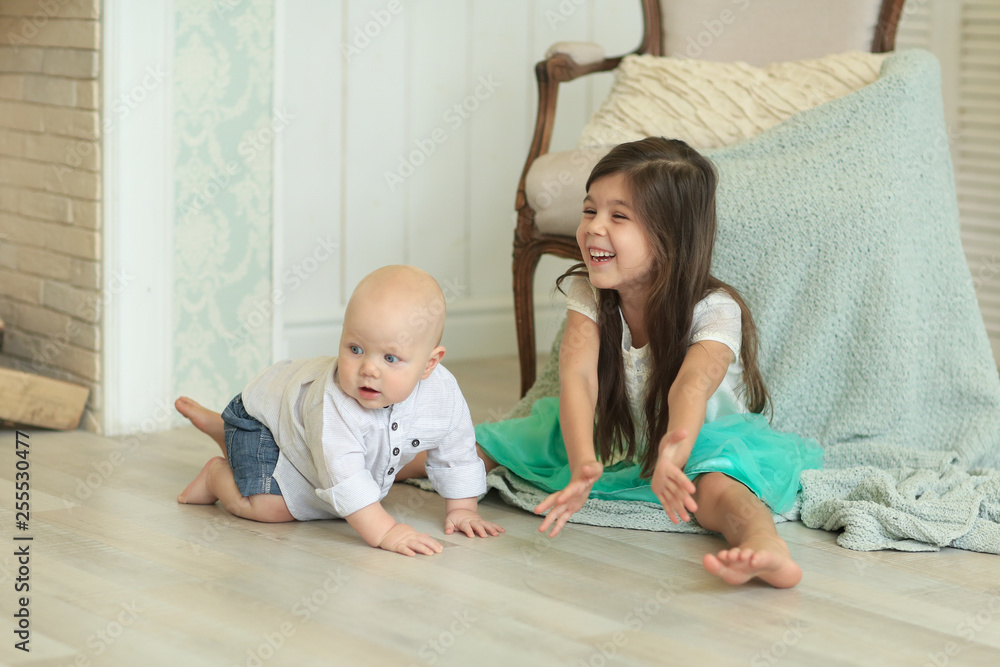 girl in a white shirt and blue skirt playing with baby brother in a white shirt and jeans sitting next to the fireplace on the floor. A family girl in a white shirt and blue skirt playing with baby brother in a white shirt and jeans sitting next to the fireplace on the floor. A family